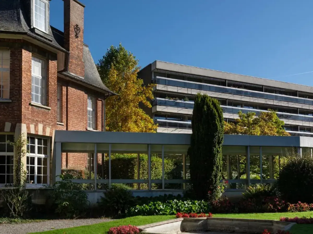 Façade de brique d’une résidence, extension vitrée ouverte sur le parc.